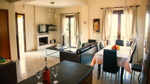 A modern living room with a sofa, dining table, and a TV. - Villa Aethra (Kefalonia)