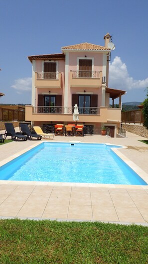 A two-story building with a swimming pool, outdoor seating, and a view of the landscape. - Villa Aethra (Kefalonia)