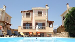 A multi-story hotel with a pool, outdoor seating, and a stone wall. - Villa Aethra (Kefalonia)
