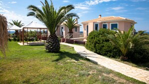 Eine Villa mit gepflastertem Weg, Palmen und Meerblick.
