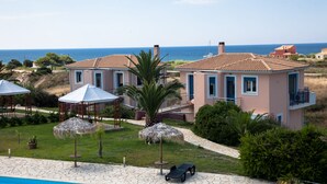 A beachfront property with a swimming pool, umbrellas, and a view of the sea.