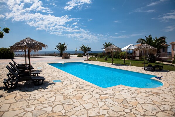 A swimming pool with stone tiles, lounge chairs, and thatched umbrellas.