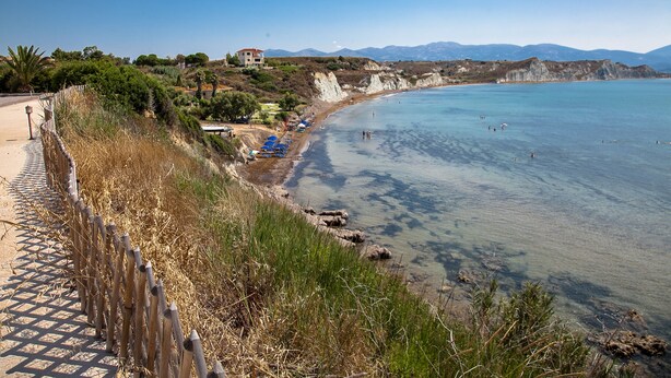 A coastal beach with clear waters, a wooden fence, and a few umbrellas.