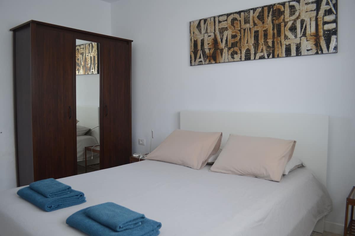 A bedroom with a bed, two pillows, a wooden wardrobe, and a wall art piece.
