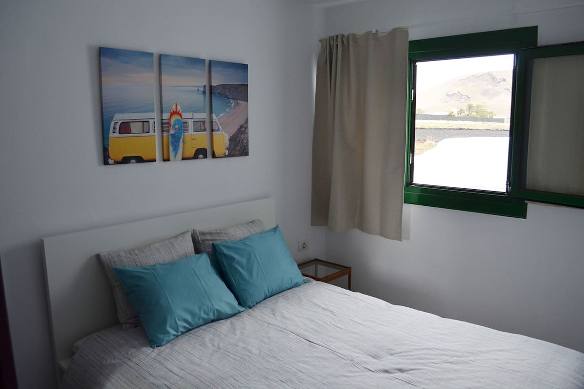 A bedroom with a bed, two pillows, a nightstand, a window with curtains, and three wall-mounted paintings.