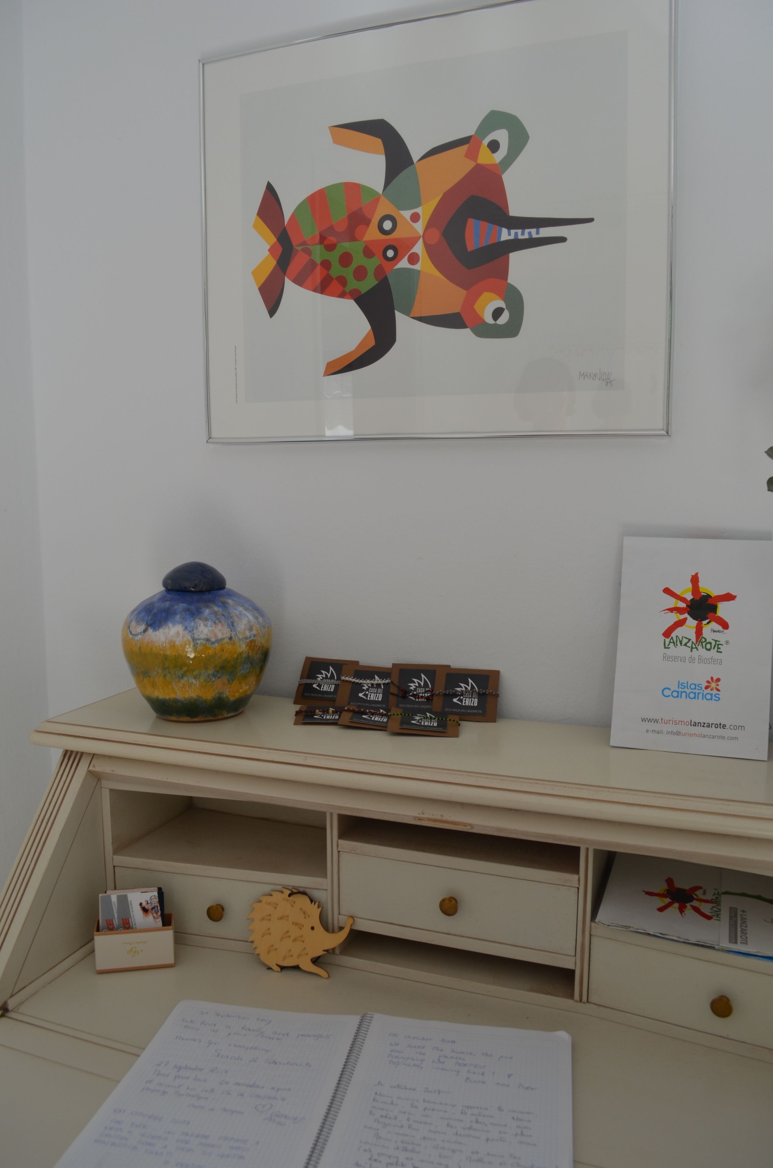 Een kamer met een bureau, een vaas, een lijst met kunstwerk en een bord.