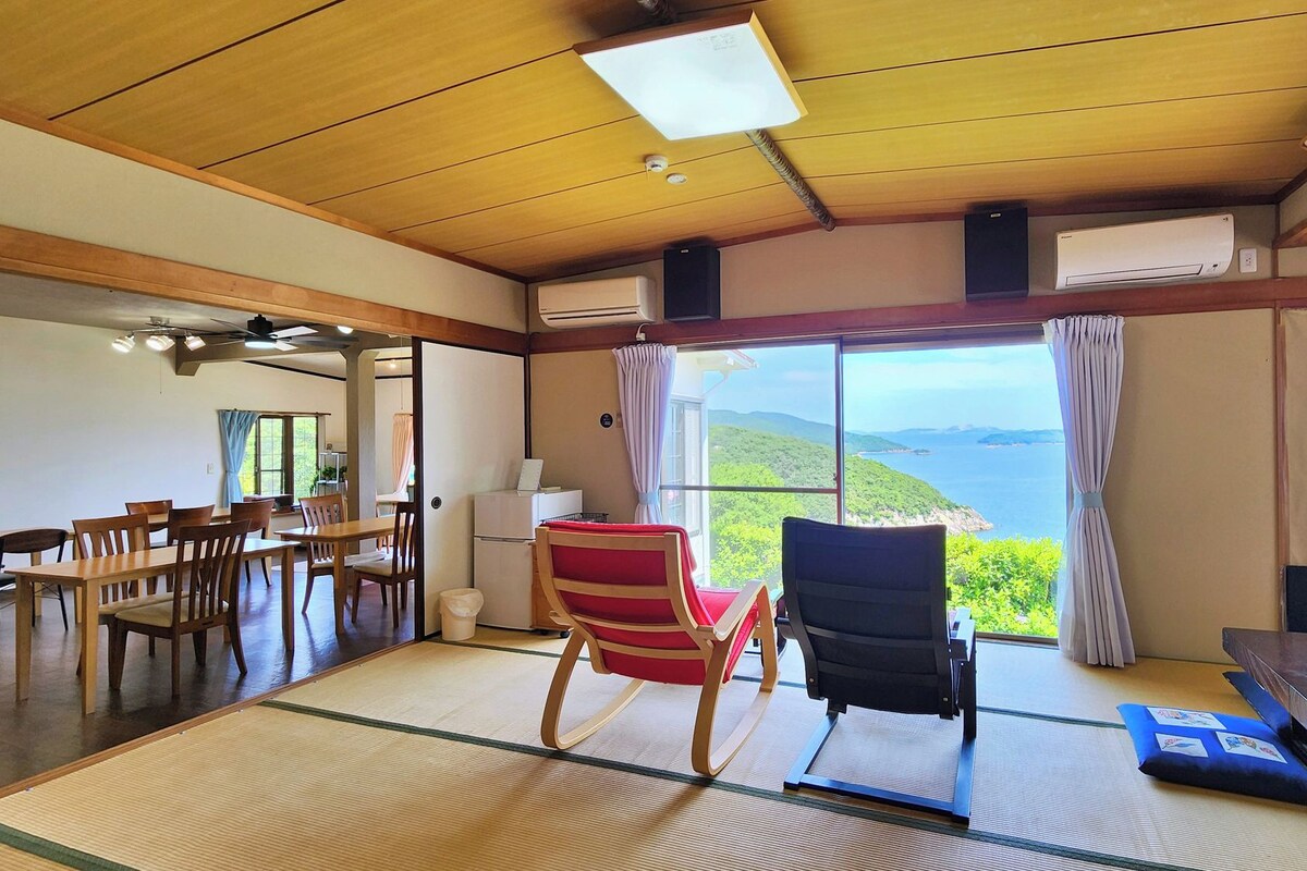 A room with a large window offering a view of the sea, a dining area with wooden furniture, and a seating area with tatami mats.