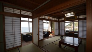 A traditional Japanese room with tatami flooring, sliding doors, a view of the sea, and a wooden table. - Furusato No Yado Kobase (Echizen)