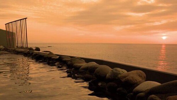 A waterfront promenade with a stone balustrade, a metal railing, and a calm sea under a sunset sky. - Furusato No Yado Kobase (Echizen)