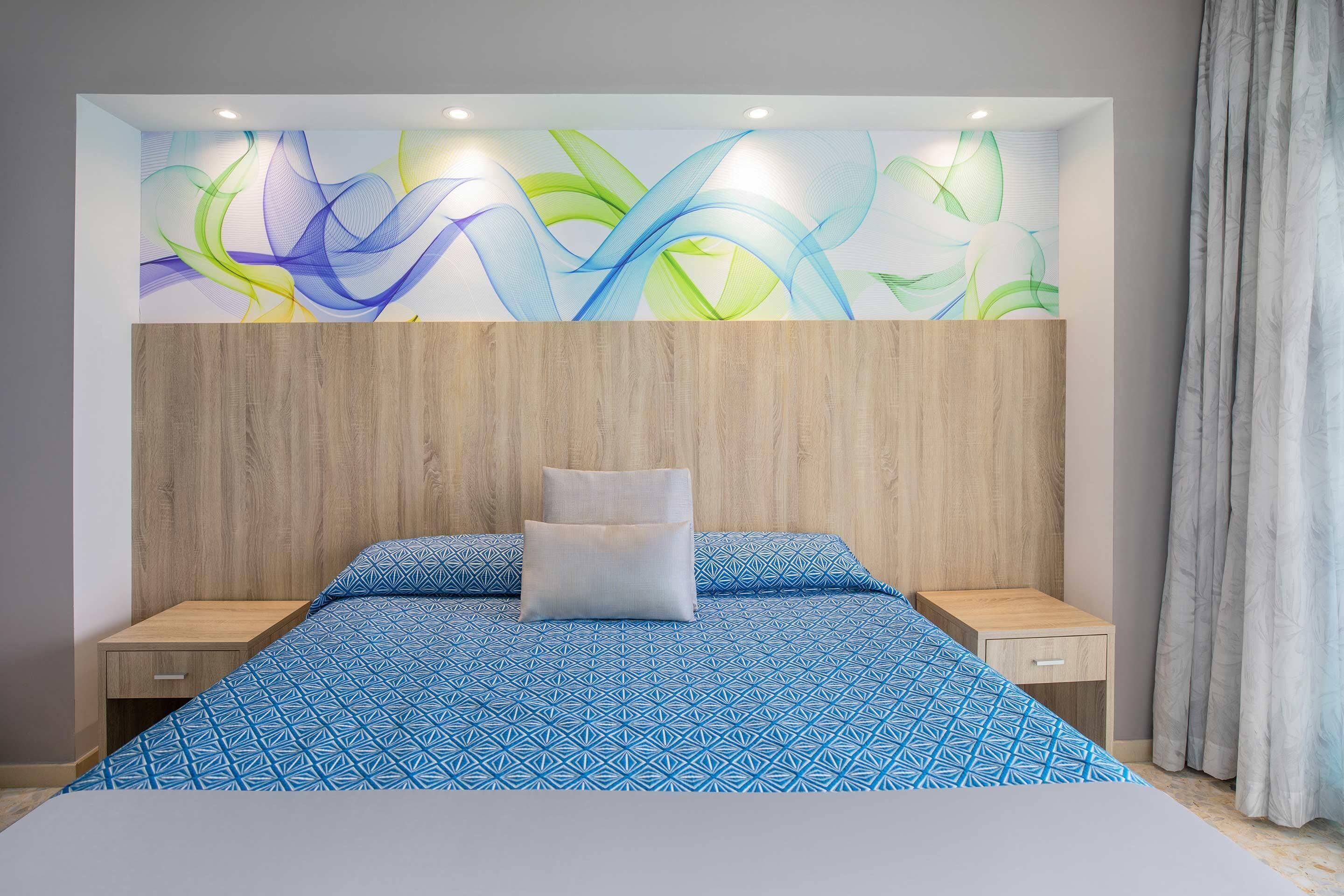 Een slaapkamer met een houten hoofdbord, een bedovertrek met blauw patroon en een wanddecoratie.