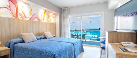 Habitación de hotel con dos camas, un escritorio y televisión. Cuenta con un balcón y vistas al mar.
