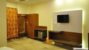 Une chambre d’hôtel avec une armoire en bois, un petit réfrigérateur, un téléviseur fixé au mur et un banc.