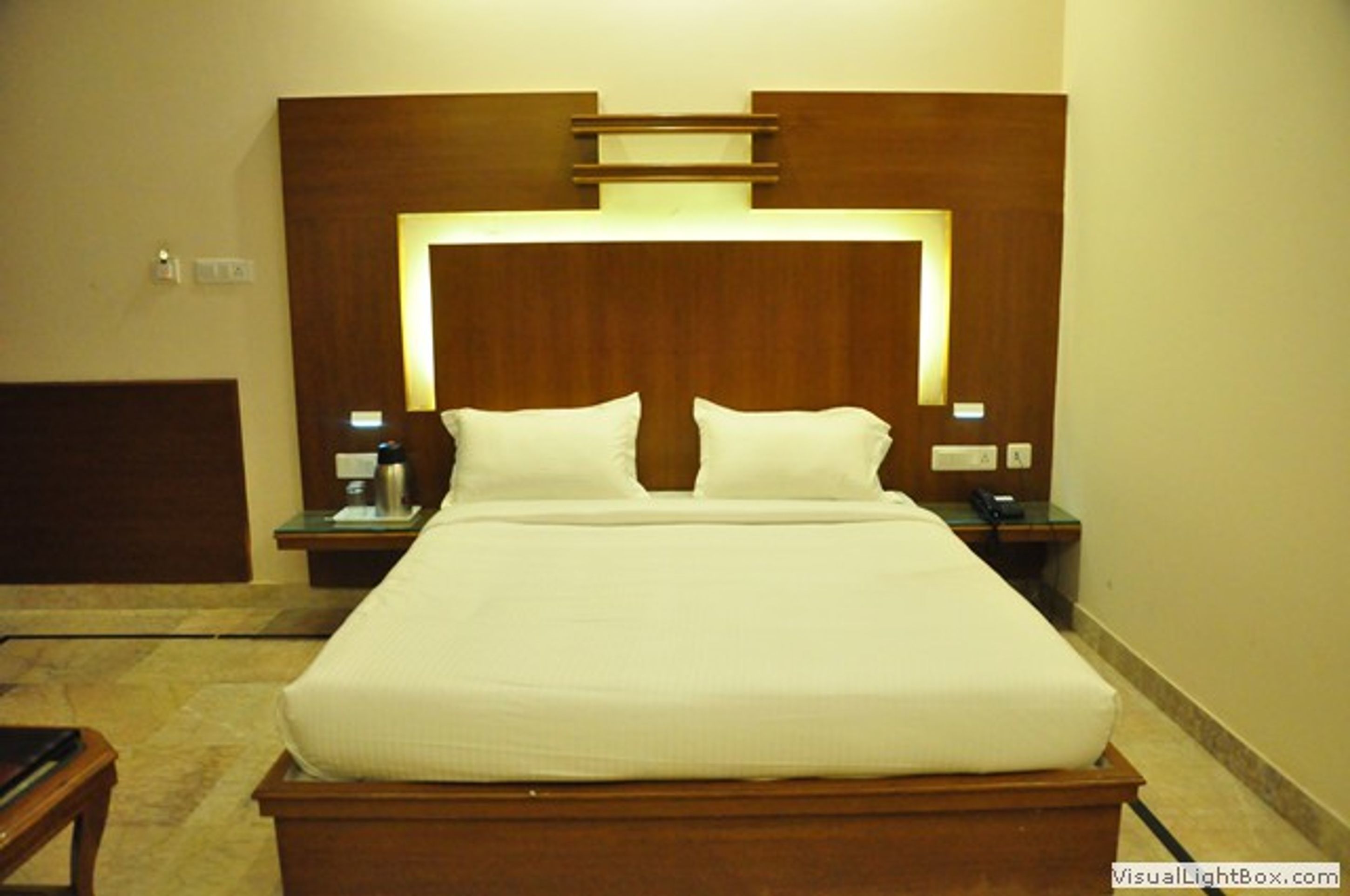 Een hotelkamer met een groot bed, houten hoofdbord, nachtkastjes en een nachtkastje met een lamp.