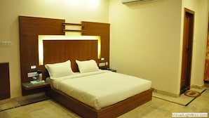Une chambre d’hôtel avec un grand lit, une tête de lit en bois, des tables de chevet, un appareil de climatisation et une petite table de nuit avec une lampe.