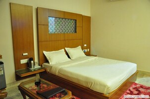 Una habitación de hotel con una cama grande, un cabecero de madera, una mesita de noche, una mesa de vidrio y un tapete rojo estampado.