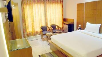 A hotel room with a large bed, a desk, two chairs, a television, and a window with curtains.