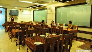 Un restaurant avec des tables et des chaises en bois, un téléviseur fixé au mur et de grandes fenêtres à vitres dépolies.