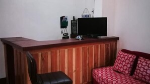 Una habitación con una barra de madera, un taburete negro, un sofá rojo estampado, un televisor y una estantería con varios objetos.