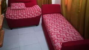Una habitación con dos camas rojas, aire acondicionado en la pared y cortinas amarillas.