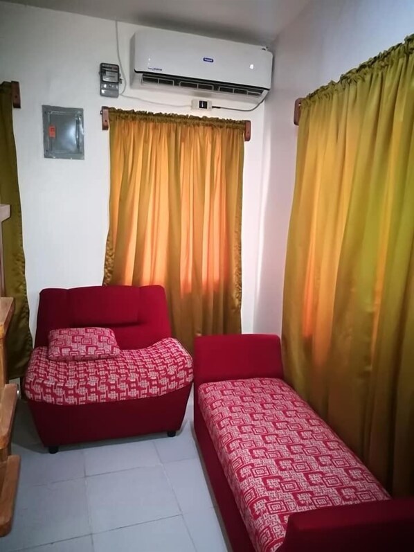 Una habitación con dos camas rojas, aire acondicionado en la pared y cortinas amarillas.