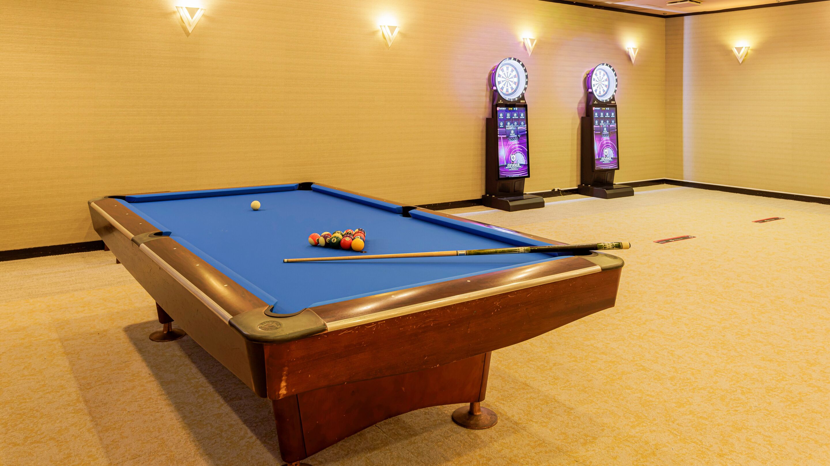 Ein Billardtisch mit Kugeln und Spielstange, ein Teppichboden und zwei Dartscheiben an einer Wand.