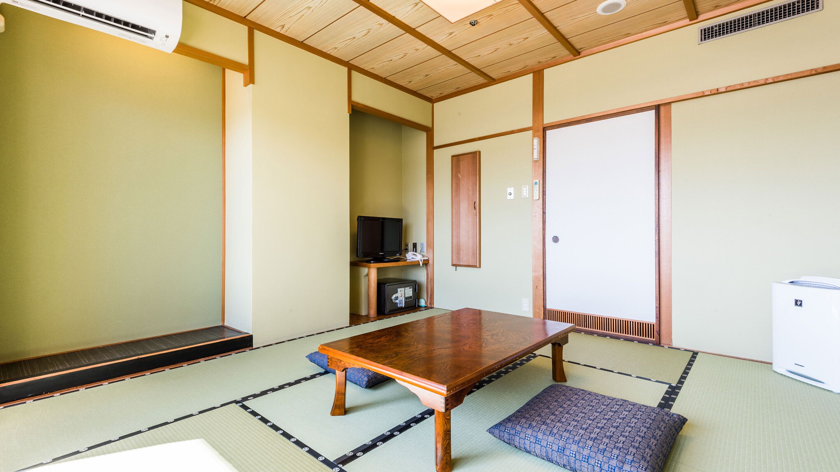 A traditional Japanese room with tatami flooring, a wooden table, a television, and a wardrobe.