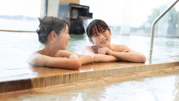Two people in a hot tub with a view of a building in the background. - Ooedo Onsen Monogatari Nagayama (Kaga)