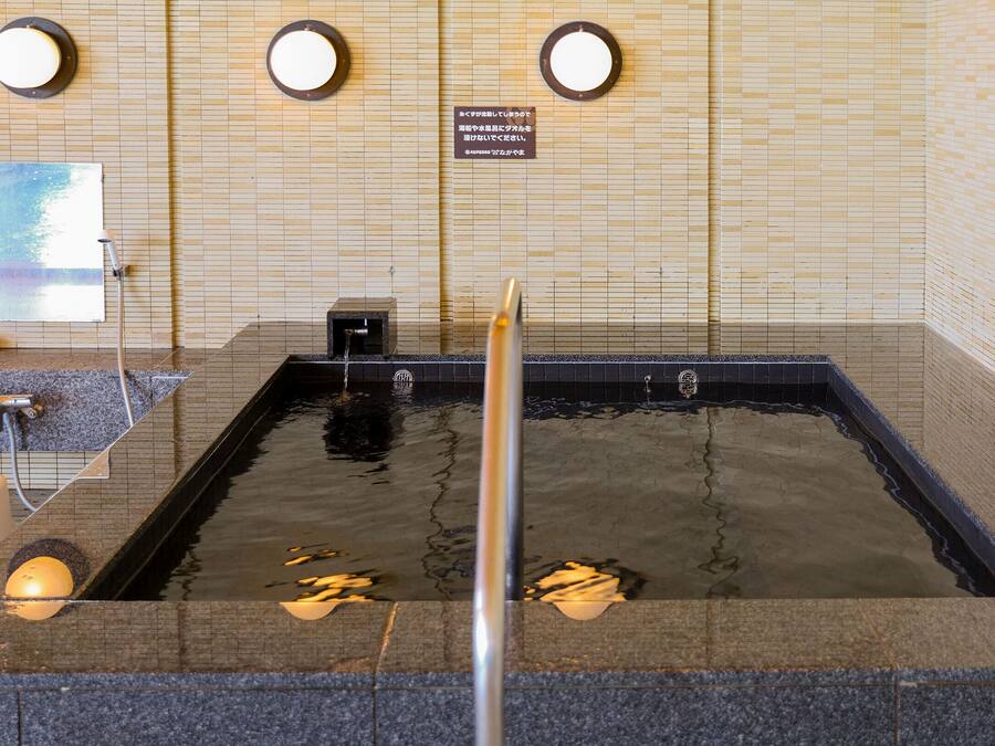 Een openlucht bad met warmwaterbron, betegelde muren en een houten vloer.