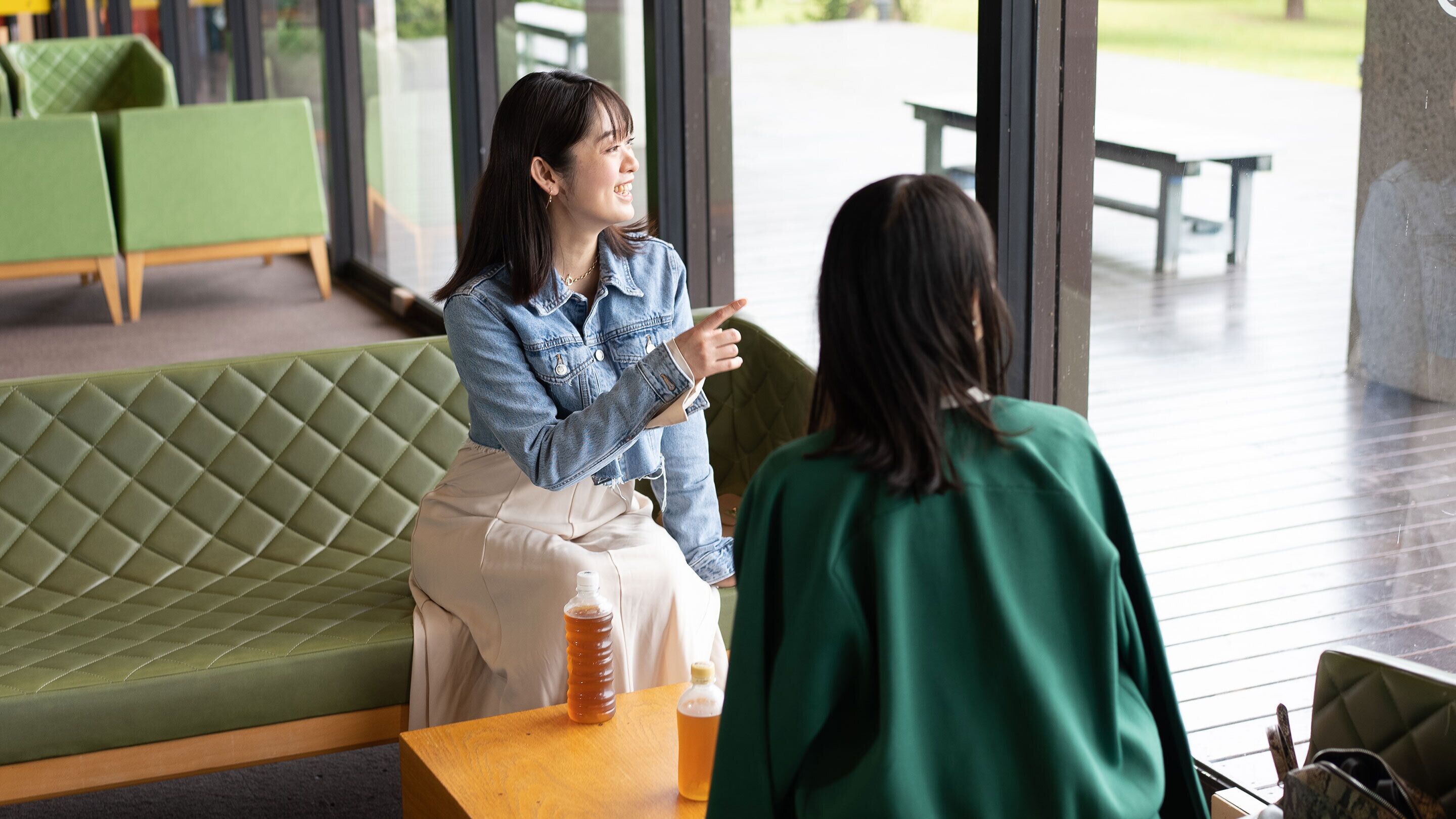 Un área de estar con asientos verdes acolchados y una mesa de madera en un espacio interior moderno.