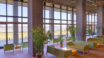 A spacious indoor area with large windows, green seating, and potted plants.