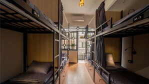 Un pasillo estrecho con literas a ambos lados, un pasillo central y una ventana con vistas a edificios.
