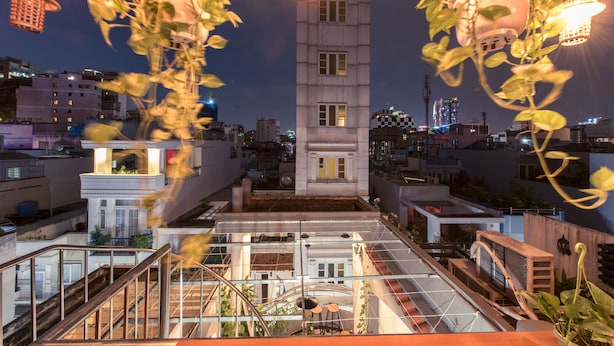 Una terraza en la azotea con barandilla de vidrio, una zona de estar central y vistas de la ciudad iluminada de noche.
