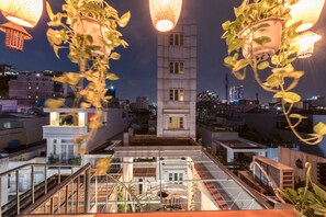 Une terrasse sur le toit dotée d’une balustrade en verre, d’un espace salon central et offrant une vue sur le paysage urbain la nuit.