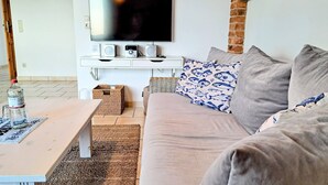 Een woonkamer met een bank, een salontafel, een televisie en speakers op een witte console.