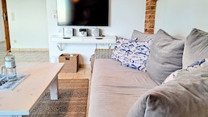 A living room with a sofa, a coffee table, a TV, and speakers on a white console.