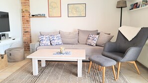 A living room with a sofa, a coffee table, a grey armchair, a television, and a bookshelf.