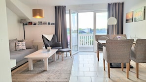 A modern living room with a sofa, a coffee table, and a dining area with wicker chairs.