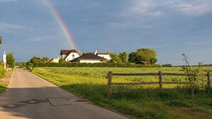 Een landweg met een regenboog, een wit huis en een houten hek.