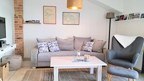 A living room with a sofa, armchair, coffee table, and a television.