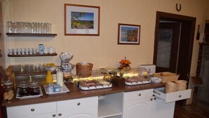 A breakfast bar with various food items and beverages, framed pictures on the wall, and a wooden door. - Pension Lachmann (Koenigstein)