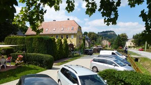 A residential street with parked cars, a yellow house, and a mountain in the background. - Pension Lachmann (Koenigstein)