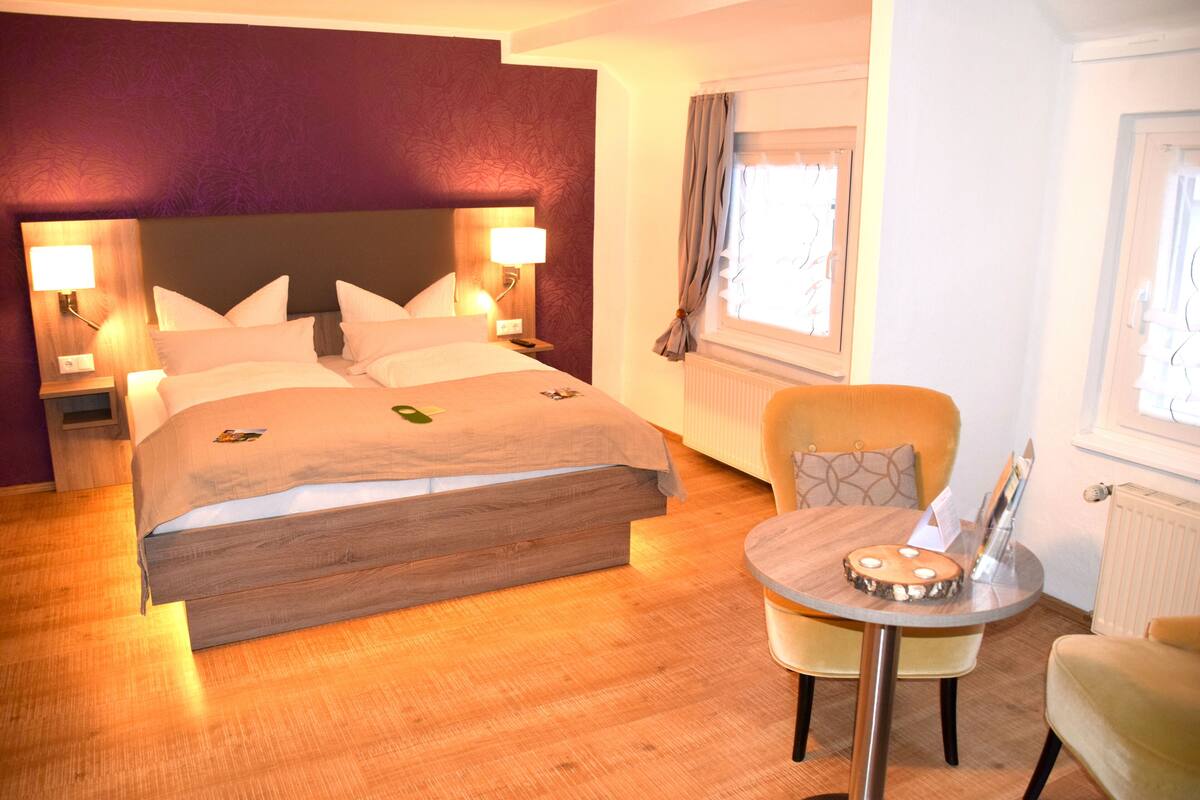 Una habitación de hotel con cama, lámparas de noche, una mesa redonda y una silla.
