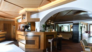 A modern bar area with a wooden counter, bar stools, and a seating area with a sofa and chairs.