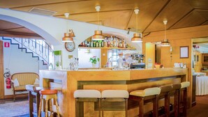 A bar area with wooden stools, a bar counter, and hanging pendant lights.