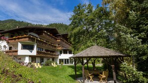 A chalet with a wooden balcony, a covered outdoor seating area, and a lush garden.