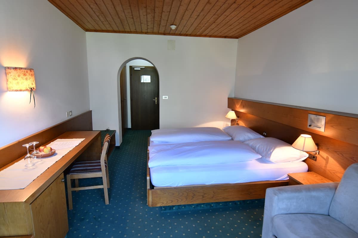 A hotel room with a wooden desk, a bed with white linens, a chair, and a lamp.