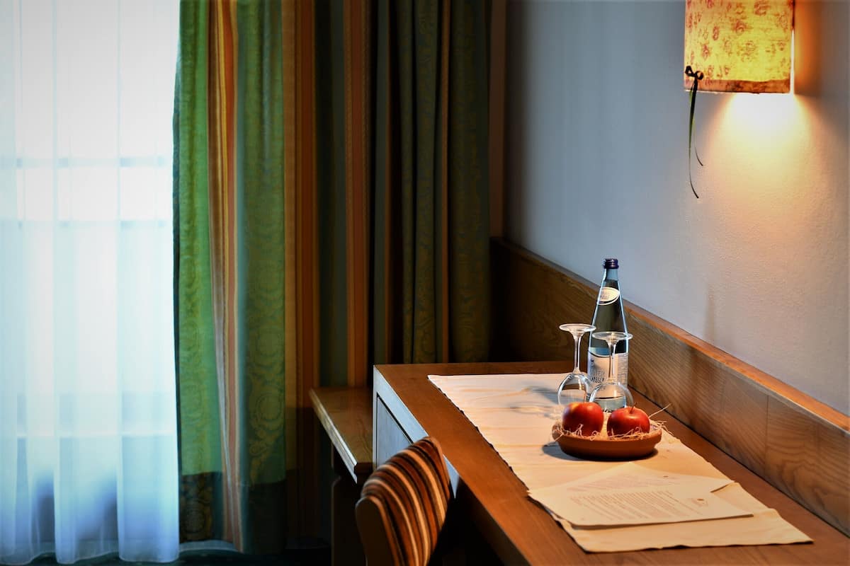 A wooden table with a bottle, glasses, and a bowl of fruit.