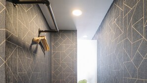 Un baño estrecho con paredes oscuras y diseños geométricos, una zona de ducha y una planta visible.