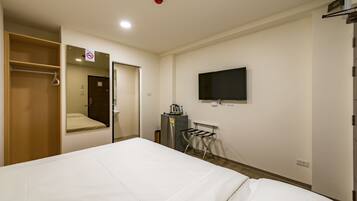 Une chambre d’hôtel avec un lit, un téléviseur fixé au mur, une armoire et une petite table avec une bouilloire.