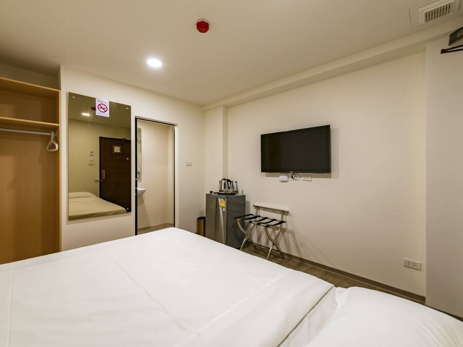 Une chambre d’hôtel avec un lit, un téléviseur fixé au mur, une armoire et une petite table avec une bouilloire.